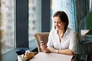 business woman in cafe smiles and writes sms phone