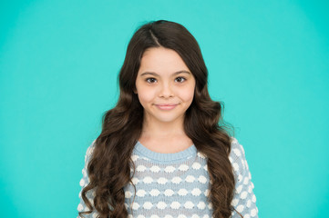 She is really cute. Happy girl child blue background. Small child wear long wavy hair. Little child with cute smile. Beauty salon. Fashion and style. Child care and childhood