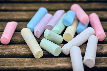 A pile of bright colorful children's street chalk on the dark wooden bars of a bench on a playground. Seen in Nuremberg, Germany, April 2019