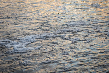 Abstract evening sunset view of small details of river waves with bubbles.
