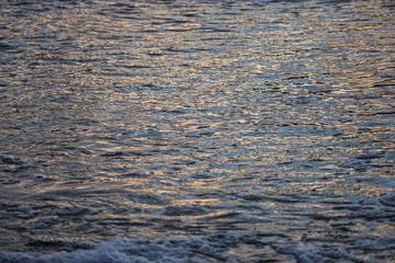 Abstract evening sunset view of small details of river waves with bubbles.