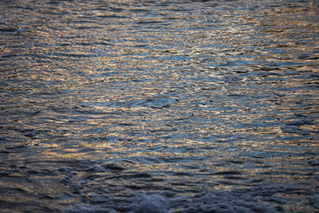 Abstract evening sunset view of small details of river waves with bubbles.