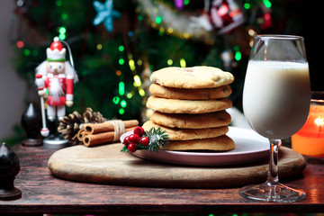 Cookies biscuits for Santa Claus near a christmas tree decorated with Nutcracker, flashing lights,mistletoe and a glass of milk on a wooden tray, atmospheric Christmas picture 