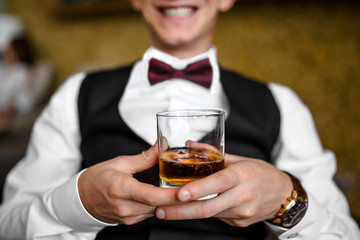 Handsome groom in white shirt sitting in luxury leather chair and holding whiskey morning before the wedding, confident business man holding cognac in glass while resting in armchair