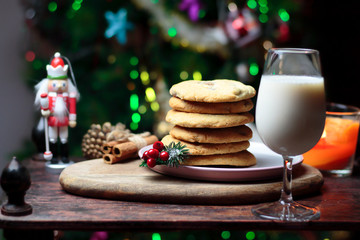 Cookies biscuits for Santa Claus near a christmas tree decorated with Nutcracker, flashing lights,mistletoe and a glass of milk on a wooden tray, atmospheric Christmas picture 
