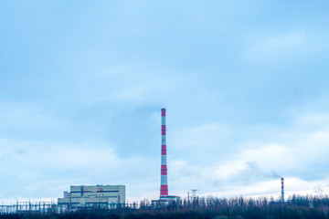 Red-white factory chimney near a winter lake.