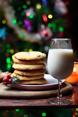 Cookies biscuits for Santa Claus near a christmas tree decorated with flashing lights,mistletoe and a glass of milk on a wooden tray, atmospheric Christmas picture