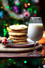 Cookies biscuits for Santa Claus near a christmas tree decorated with flashing lights,mistletoe and a glass of milk on a wooden tray, atmospheric Christmas picture