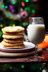 Cookies biscuits for Santa Claus near a christmas tree decorated with flashing lights,mistletoe and a glass of milk on a wooden tray, atmospheric Christmas picture