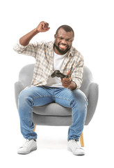 Obraz premium Emotional African-American man playing video game while sitting in armchair against white background