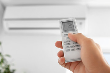 Young man switching on air conditioner at home, closeup