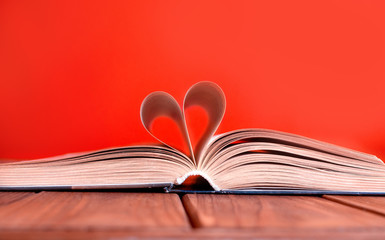 Open book on wooden table on red background