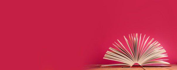 Open book on wooden table on red background