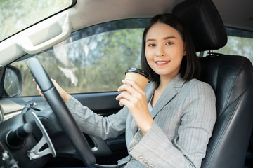 Fototapeta na wymiar Asian female driver smiling and drinking coffee in the car, Beautiful girl holding an eco paper coffee cup,looking to camera while driving her car, happy life transport in city