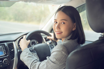 Safety driving concept, Smiling happy young  Chinese Thai Asian businesswoman driving a car in town, Confident and beautiful girl. Rear view  woman in business suit wear looking over her shoulder