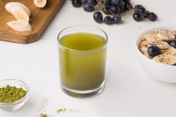 green matcha tea next to oatmeal, banana and grapes on a white background. Healthy vegan breakfast concept