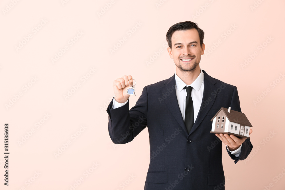 Wall mural Male real estate agent with key and model of house on color background