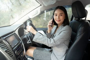 Asian woman talk by mobile calling texting and looking on a cellular phone while sitting in her car, driving under the influence, the driver is safely talking by smartphone in a car concept