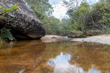 Clear water on a plateau rock formation reflecting the natural surrounding part of a slow cascading waterfall with a huge black granite rock and vegetation in the background near Ouro Preto, Brazil