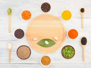 Fototapeta na wymiar Round kitchen cutting board and ingredients for cooking: black pepper, turmeric, chili, green grass, masala, cumin (jeera), cardamom, carrot, dry onion, herb, salt. Healthy eating concept