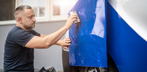 Werbetechniker foliert ein Auto mit blauer Folie	