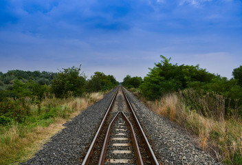 Fototapeta na wymiar Train tracks, straight road, travel in nature. Vivid natural colors of suburban landscape