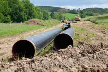 Gas pipeline laying on the countryside with two gas pipeline pipes in the foreground and machines for pipe laying along with other pipes in the background