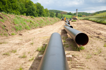 Gas pipes are shown in large format in a country side with pipe laying equipment in the background
