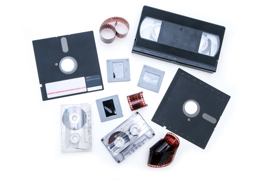 A group of old retro audio visual equipment used to capture or record  pictures, video, audio or data. The floppy disc, audio and video cassettes, film strip and  slides. 