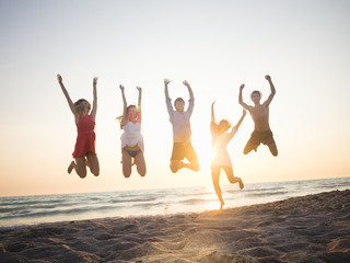 Five friends jumping on the beach at sunset on summer
