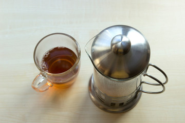 Transparent mug with tea, metal french press kettle, top view, wooden table. Minimalization