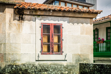 old wooden window on a moss-covered rustic facade with a tiled roof in a village