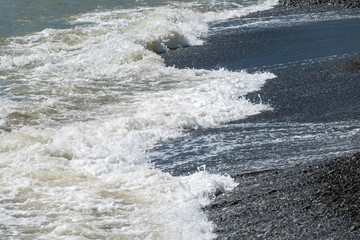 Sea water with foam on a pebble beach.