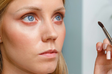 Obraz premium The process of creating makeup. Makeup artist working with a brush on the face of the model.