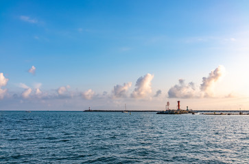 Sea harbor with breakwater and lighthouse at sunset.