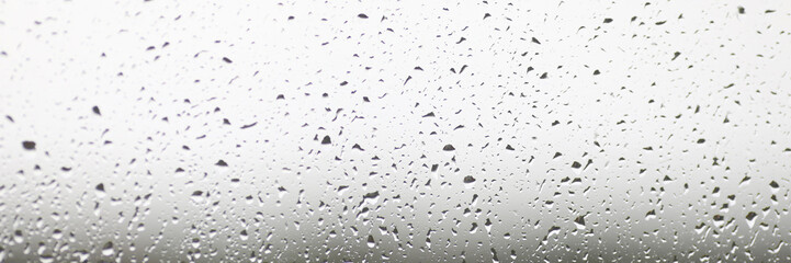 Close-up on window stained with autumn rain. Abstract texture with falling raindrops. Condensation on clear windowpane or transparent surface. Blurred background
