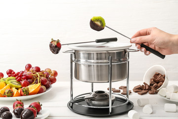 Woman dipping tasty fruits into bowl with chocolate fondue on table