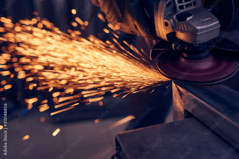 Wall mural Worker cutting metal with grinder. Sparks while grinding iron