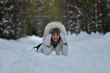 Beautiful girl in the winter frosty forest lies in the snow