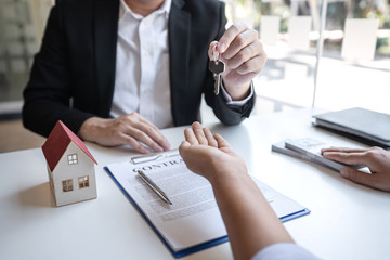 Real estate agent are presenting home loan and giving house, keys to customer after signing contract to buy house with approved property application form