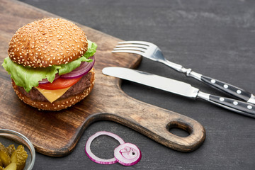 delicious fresh cheeseburger on wooden board near cutlery