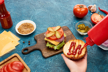 cropped view of woman cooking delicious fresh burger on blue textured surface