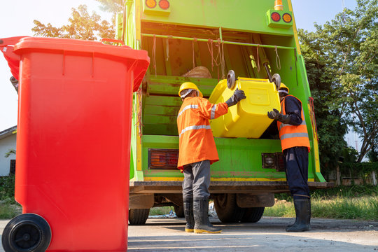 Two garbage men working together on emptying dustbins for trash removal with truck loading waste and trash bin.