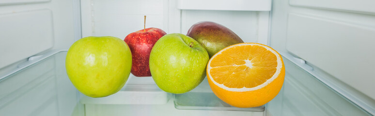Panoramic shot of fresh mango with apples and orange slice on refrigerator shelf