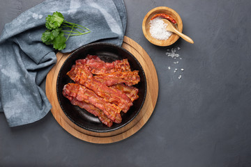 Crispy fried bacon in a cast iron pan on a gray background.