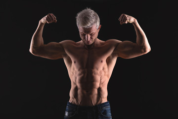 Fototapeta na wymiar Handsome power athletic man in dramatic light. Strong bodybuilder with perfect shoulders, biceps, triceps, back, delta and chest. Strength and motivation