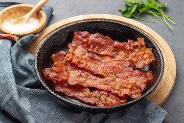 Crispy fried bacon in a cast iron pan on a gray background.