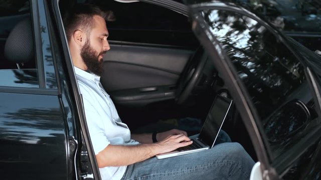 A car is black. A man is writing an email. He is sitting in the car.