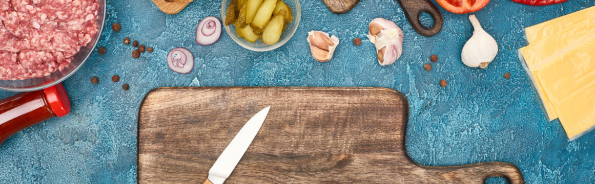 Top View Of Fresh Burger Ingredients And Wooden Cutting Board With Knife On Blue Textured Surface, Panoramic Shot