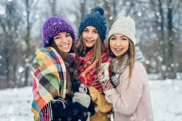 Three women friends outdoors in knitted hats having fun on a snowy cold weather. Group of young female friends outdoors in winter park.